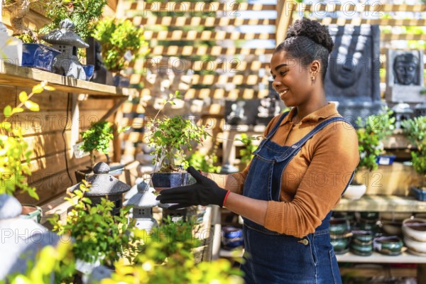 Smiling young woman working in a vibrant plant shop, holding a small bonsai tree and showcasing her
