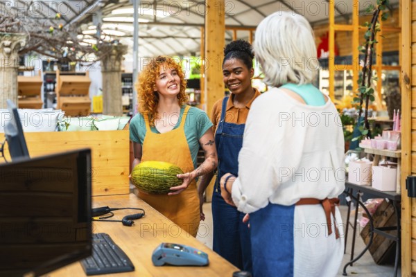 Two young shop assistants engaging with a customer while showcasing a fresh melon in a vibrant