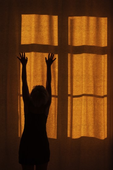 Back view of a woman with raised hands standing in front of a window with a red curtain