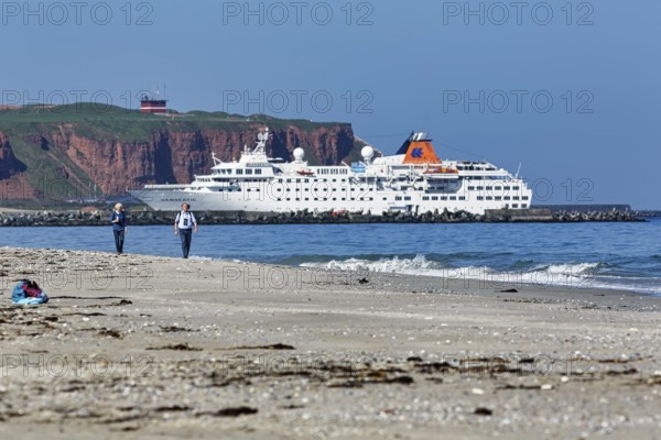 Tourists and photographers on the beach of the Heligoland dune, cruise ship in front of cliffs,