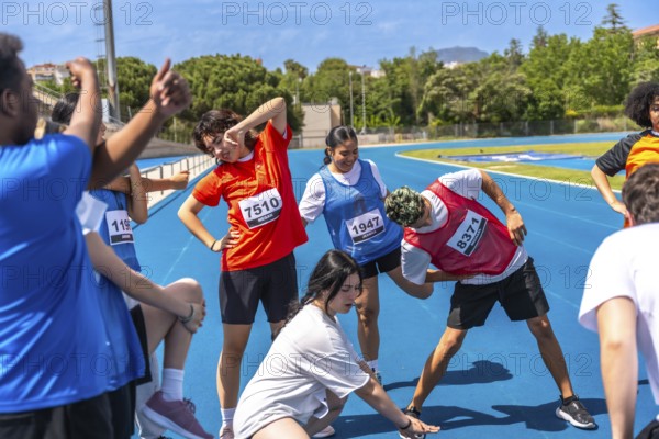Teenagers wearing bib numbers stretching together on a blue running track before a track and field