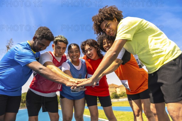 Diverse group of athletes gathers on a running track, joining hands in a circle, symbolizing