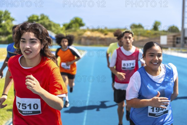 Teenage track and field athletes running on a blue track during a competition, wearing bibs with