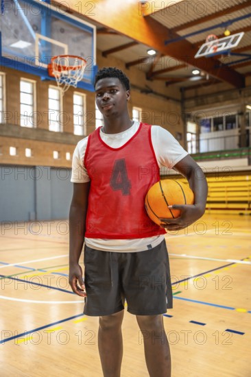 Young male basketball player holding a ball while standing confidently on a polished wooden court