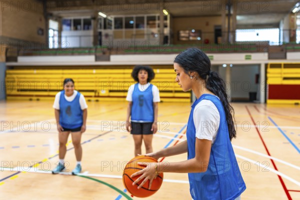 Young woman basketball player holding a ball while practicing with her team on the court in a gym,