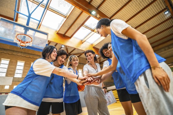 Female basketball players and their coach stacking hands, demonstrating teamwork and unity before a