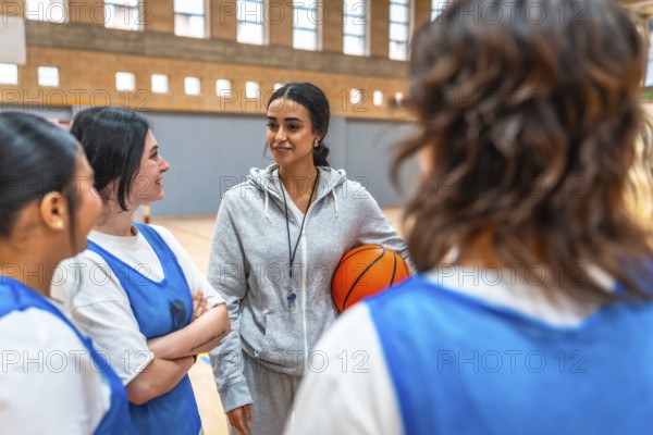 Female basketball coach holding a ball and engaging with her team during an intense training