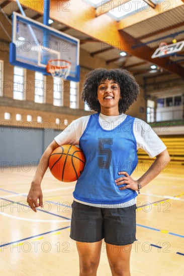 Young woman basketball player smiling while holding a ball on the court, exuding confidence and