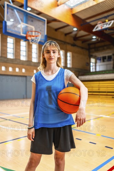 Young female basketball player standing on the court, holding a basketball, ready for the game,