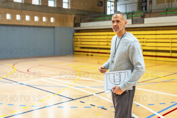 Mature basketball coach holding clipboard with game strategy explaining tactics to team players in