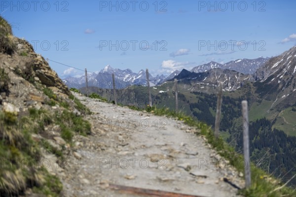 Stony hiking trail along a fence with a mountain backdrop and blue sky