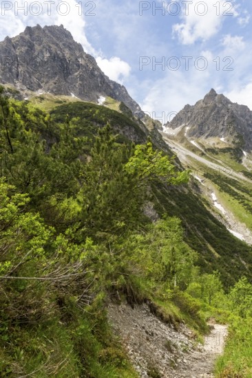 Stony path in an alpine mountain landscape under a blue sky with clouds and a view of the small and