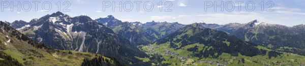 An expansive mountain panorama with green valleys under a partly cloudy sky with a view of the Hohe