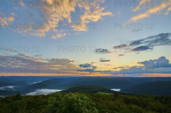 Sunrise with dramatic clouds behind wooded hills, golden light in the sky, Katzenbuckel, Waldbrunn,