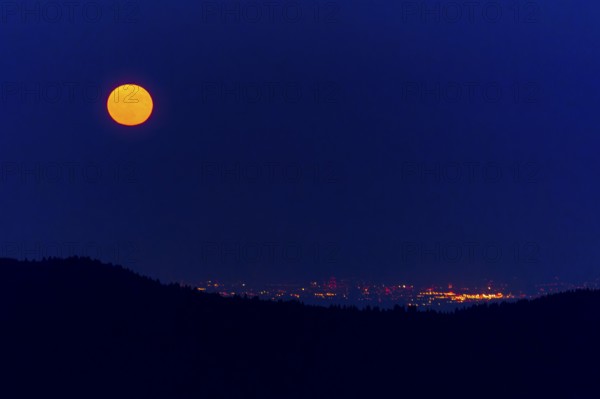 Full moon over a city with sparkling lights at night, full moon, strawberry moon 2025, Vosges,