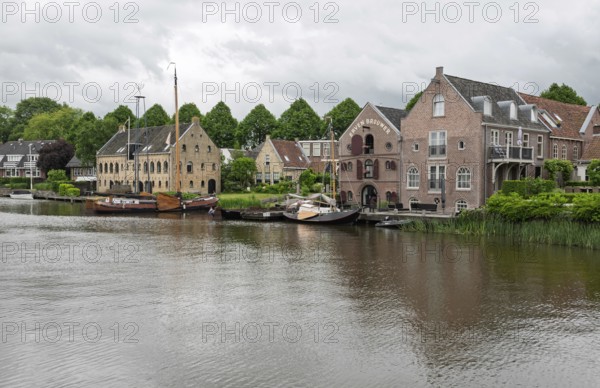 Tranquil river landscape with boats and brick buildings under a cloudy sky, Dokkum, Friesland,