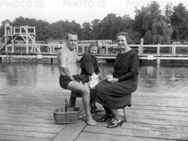 Picnic in outdoor swimming pool, family sitting on a jetty by the lake, relaxing in summertime,