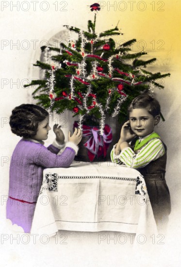 1920, 2 children under a Christmas tree, Two children decorating a small Christmas tree on a table,