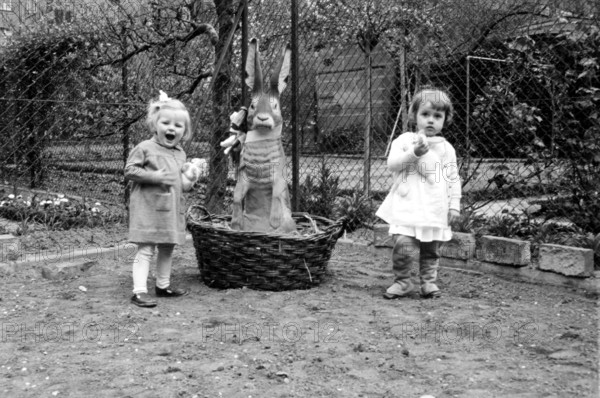 Easter bunny basket girl, 1920, Two small children standing in a garden next to a large basket with
