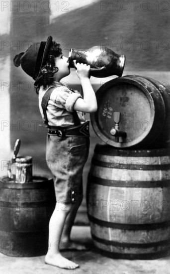 Child drinking wine, 1910s, A boy in traditional dress drinks from a large jug next to beer