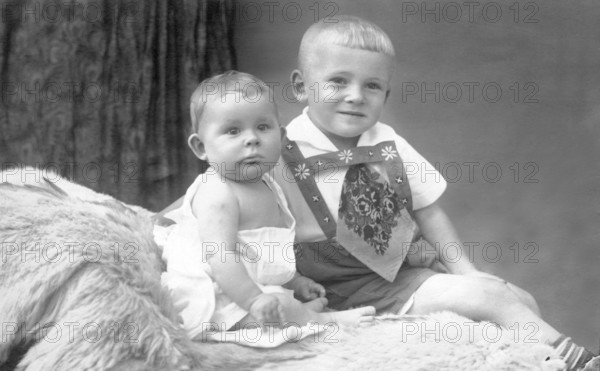 Two little boys on bed, 1930s, An older child holding a baby sitting on fur in a studio portrait,