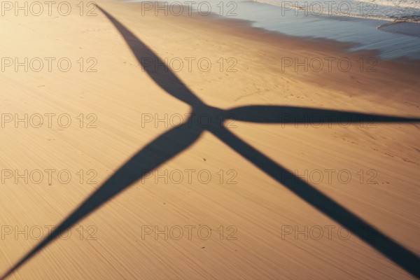 Wind turbine shadow on sunlit beach. A poetic symbol of clean energy blending with nature.