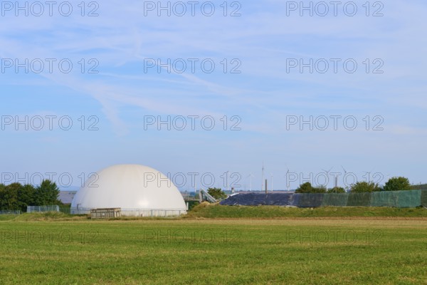 Biogas plant with wind turbines in the background, wide green field, Germany