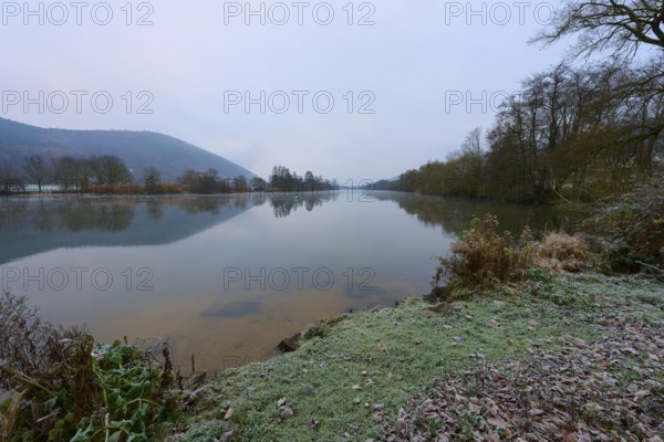 A calm winter river, with frozen banks and bare trees in the background, Laudenbach, Main,