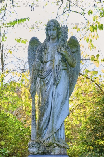 Angel made of stone with sword in an autumnal setting, surrounded by colourful leaves, cemetery,