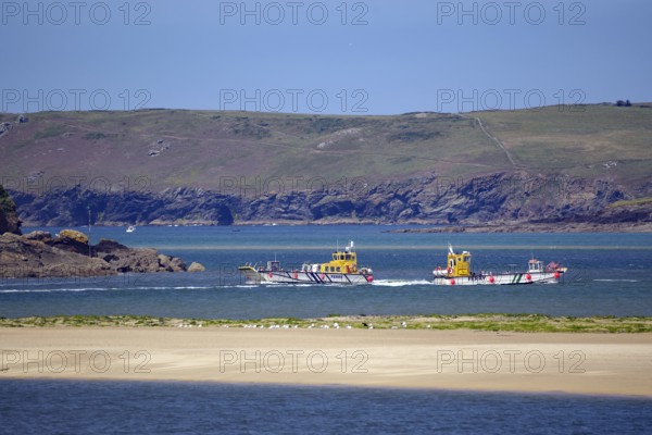 Two small passagi in blue water against a rocky coastline and green cliffs, Camel Trail, Padstow,