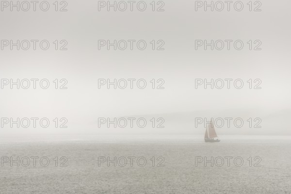 A sailing boat is travelling on the ocean on a cloudy day. The sky is overhanging and the water is