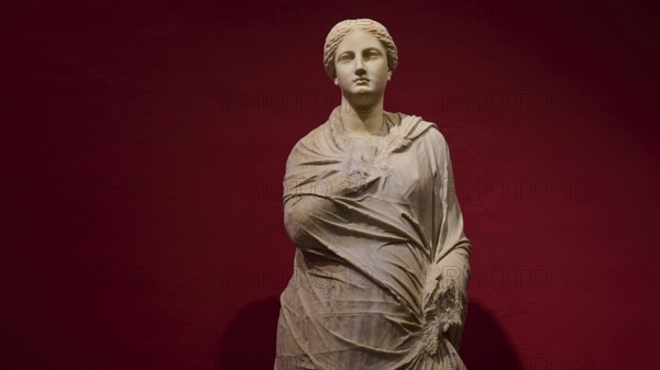 Marble statue of a woman in draped shawls, depicted against a red background, Archaeological