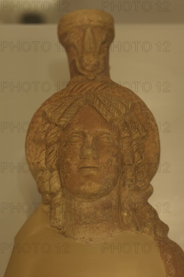 Ancient stone figurine head with elaborate hairstyle, placed on an exhibition shelf, sun disc,