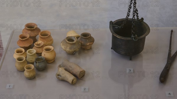 Collection of ancient ceramic artefacts, various pots and a metal crucible on display,