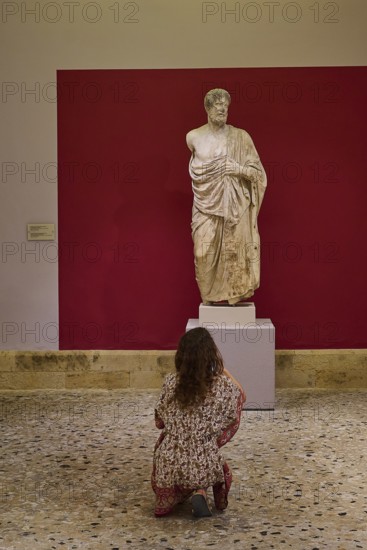 Woman observing an ancient marble statue of a man in a museum, Archaeological Museum, Kos Town,