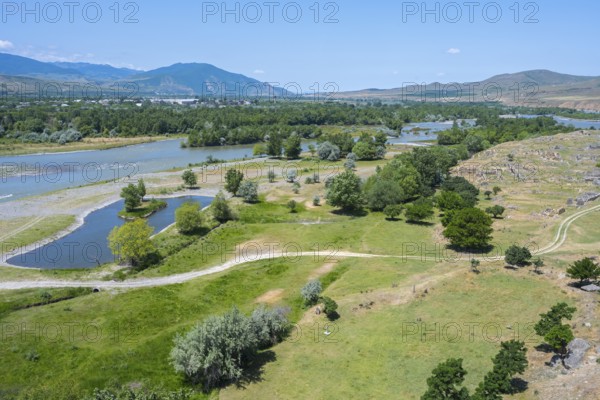 Wide landscape with river, green fields and hills under a blue sky, view from the cave town of