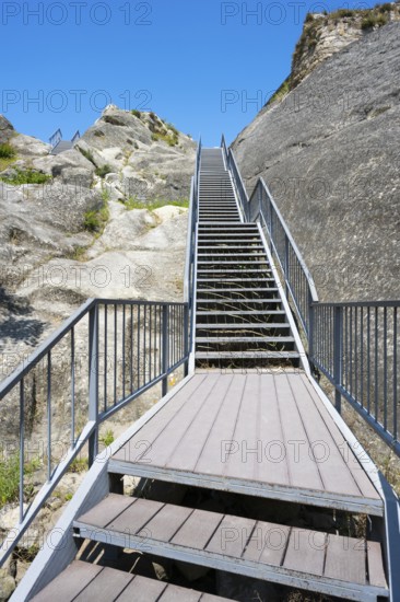 Metal staircase leads up between rocky walls under blue sky, Uplistsikhe cave town, Uplistsikhe,