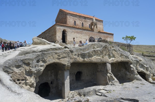 Historic church on a rock with caves and tourists on a clear day, 10th century princely church,