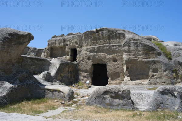 Ancient rock structure with several cave entrances in natural surroundings, Uplistsikhe cave town,