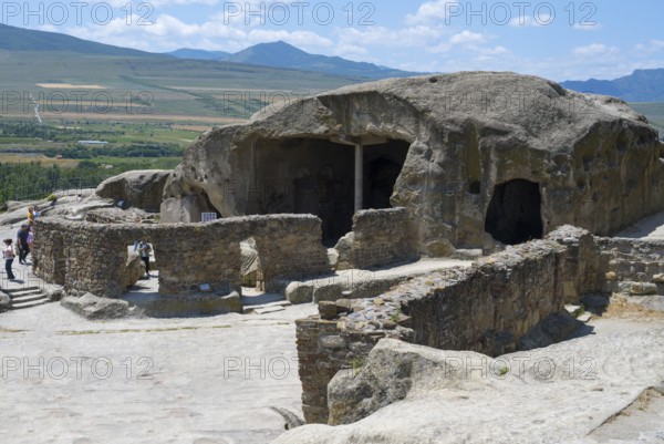 Ancient cave system with ruins in a vast landscape, visitors explore, Tamaris Darbasi, Tamaras