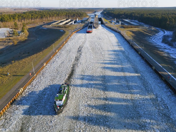 A ship sails through a long, icy waterway lined with locks in a wide landscape, aerial view,