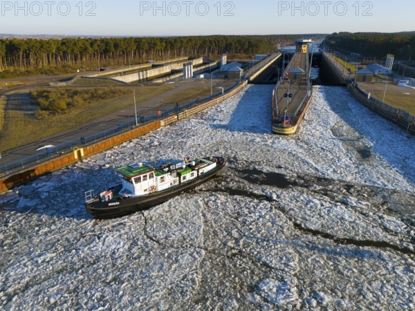 A ship navigates through an ice-covered channel in front of a lock in a wintry landscape with