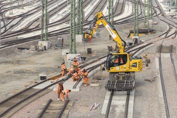Construction workers work with a crane truck on a section of rail in a large track area,