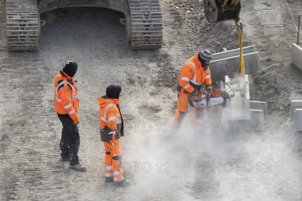 Construction workers in protective clothing work with machines on a dusty construction site,