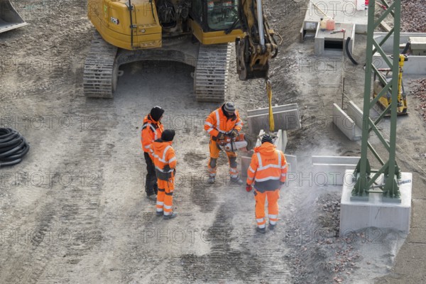 Workers wearing safety clothing use cutters near excavators on construction site, Untertürkheim