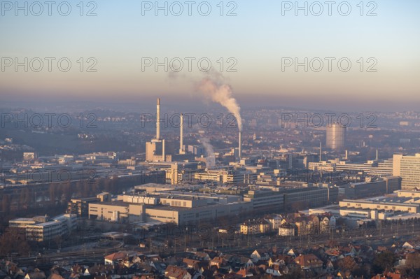 City view at dusk, modern buildings in the foreground, chimneys with smoke and a calm atmosphere in