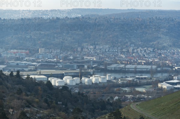 Industrial plant with white tanks in front of a hilly landscape covered with houses, view of