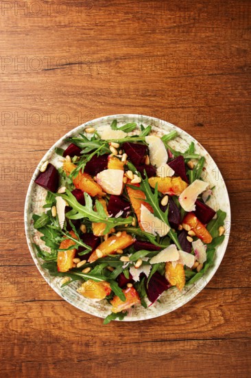 A bowl of salad contains beetroot, orange slices, pine nuts, and leaves. It is placed on a wooden