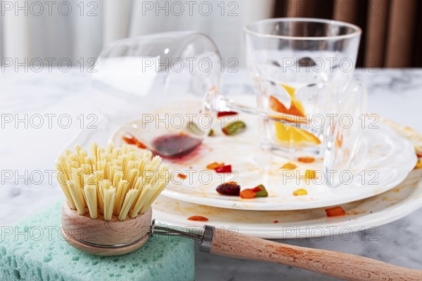 Dishes are stacked on a kitchen counter with food remnants after a meal. A cleaning brush and