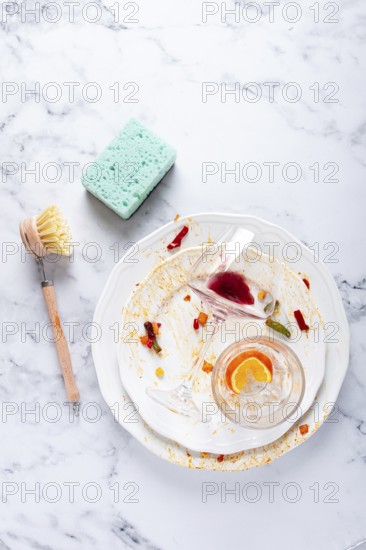 Dishes are stacked on a kitchen counter with food remnants after a meal. A cleaning brush and